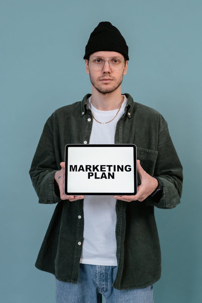 about-01 A man in casual attire displays a tablet with Marketing Plan text against a blue background.
